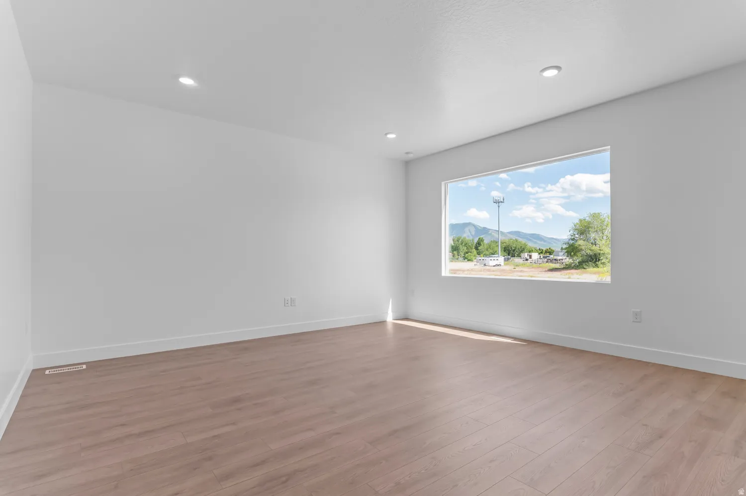 Recessed lighting, light wood-finish flooring, a rectangular window, and white walls