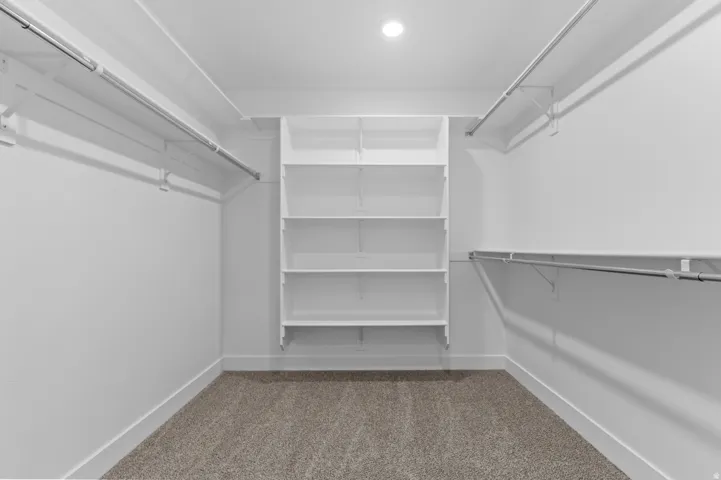 Recessed lighting illuminates the walk-in closet, featuring a built-in shelving unit, dual clothing rods, and carpet flooring