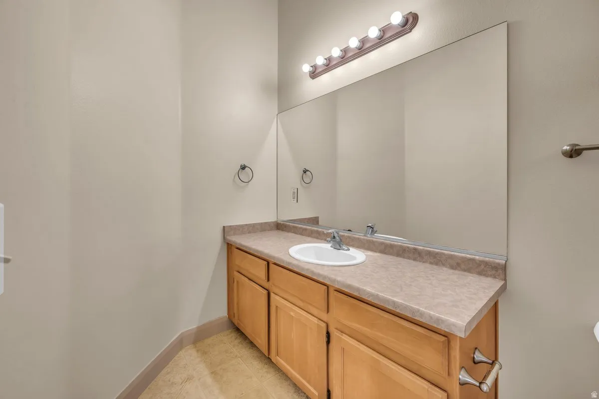 Bathroom vanity featuring a light wood-finish cabinet with double doors and three drawers, a neutral countertop, and an integrated white sink with a chrome faucet