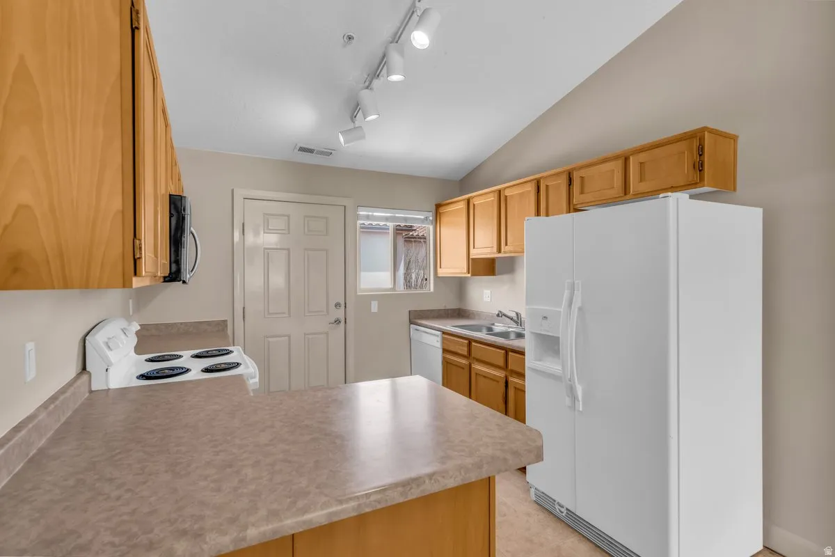 Kitchen featuring light wood cabinetry, laminate countertops, track lighting, and a paneled entry door