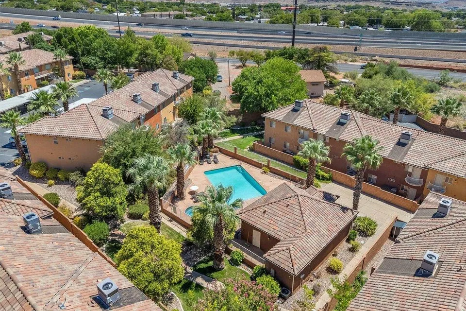 Community pool area with surrounding stucco buildings featuring tile roofs, mature palm trees, and landscaping