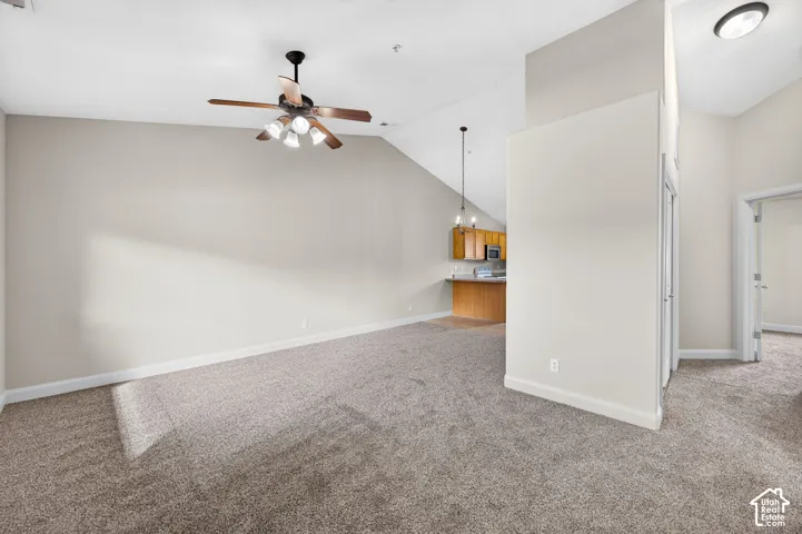 Vaulted ceilings with a ceiling fan, neutral carpeting, light-colored walls, and a built-in kitchen bar with wood-finish cabinetry