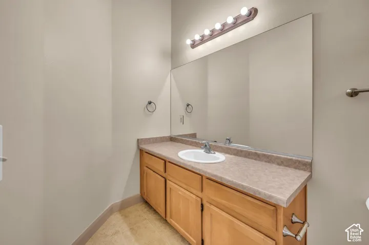 Wood-finish cabinetry with brushed nickel hardware, laminate countertop with integrated sink, large vanity mirror, and overhead strip lighting