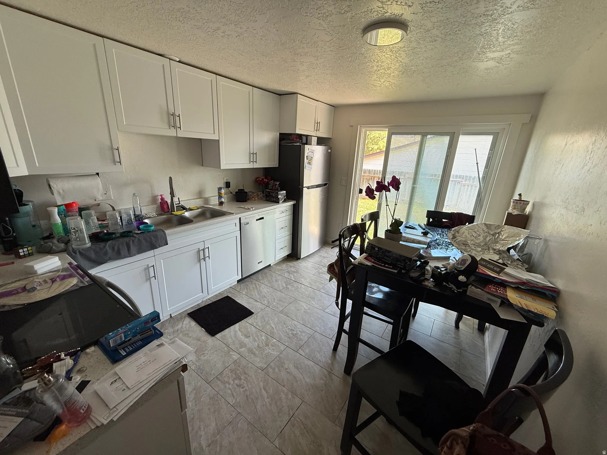 Kitchen with light countertops, white cabinetry, a textured ceiling, stainless steel appliances, and a textured wall