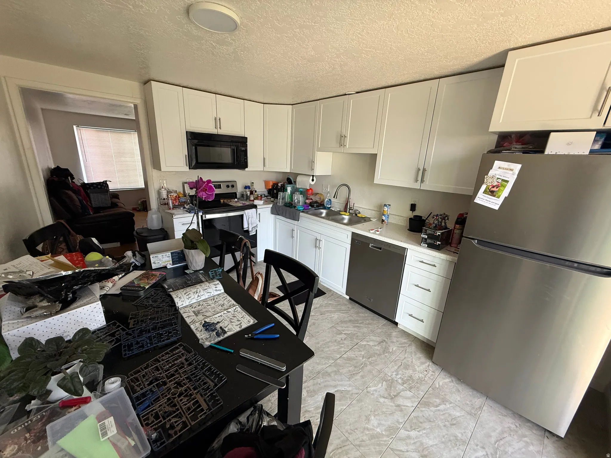 Kitchen with stainless steel appliances, white cabinets, light countertops, and a textured ceiling
