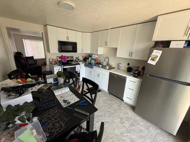 Kitchen with stainless steel appliances, white cabinets, light countertops, and a textured ceiling