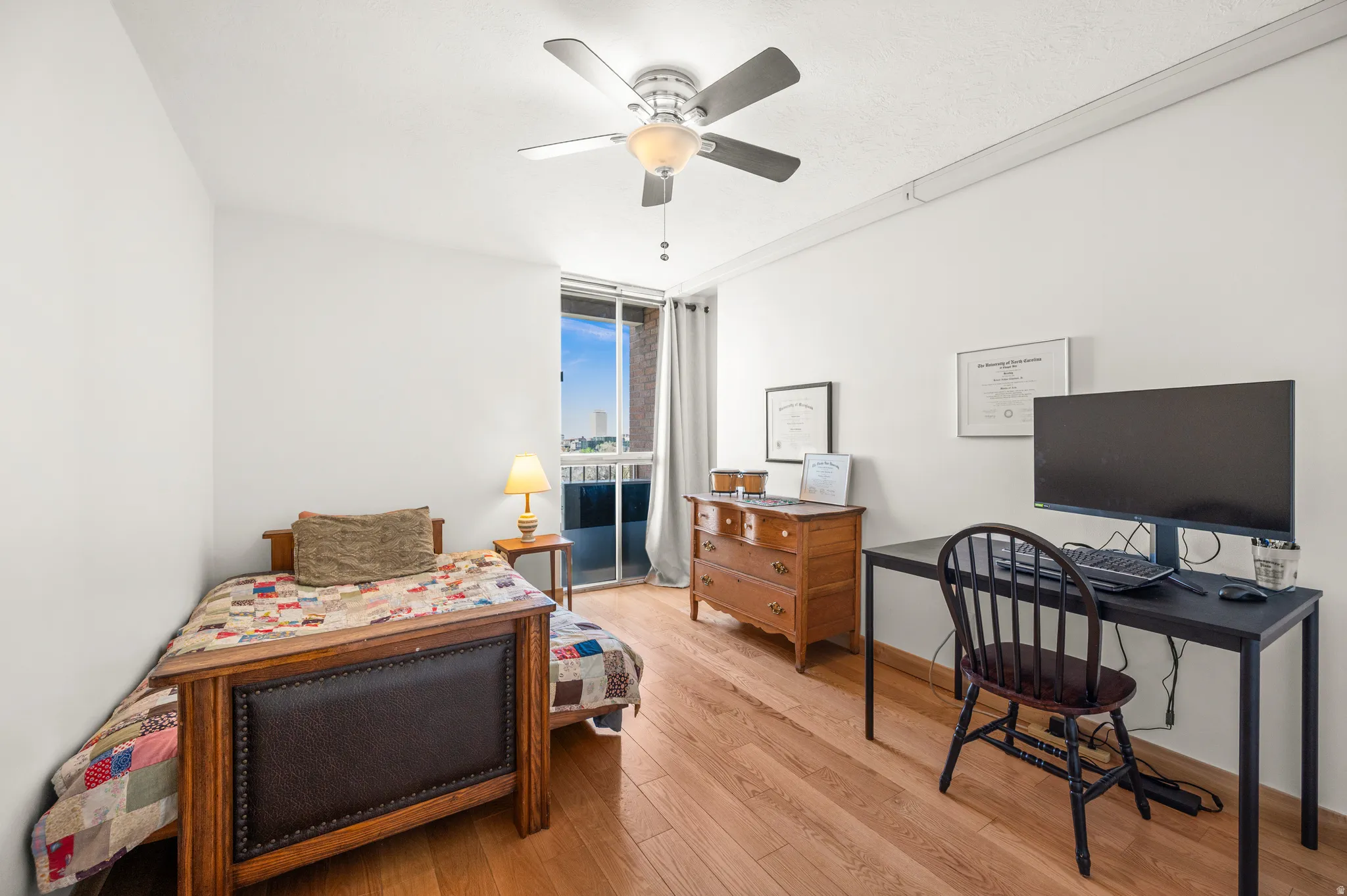 Bedroom with light wood-style floors, ceiling fan, floor to ceiling windows, and an office area