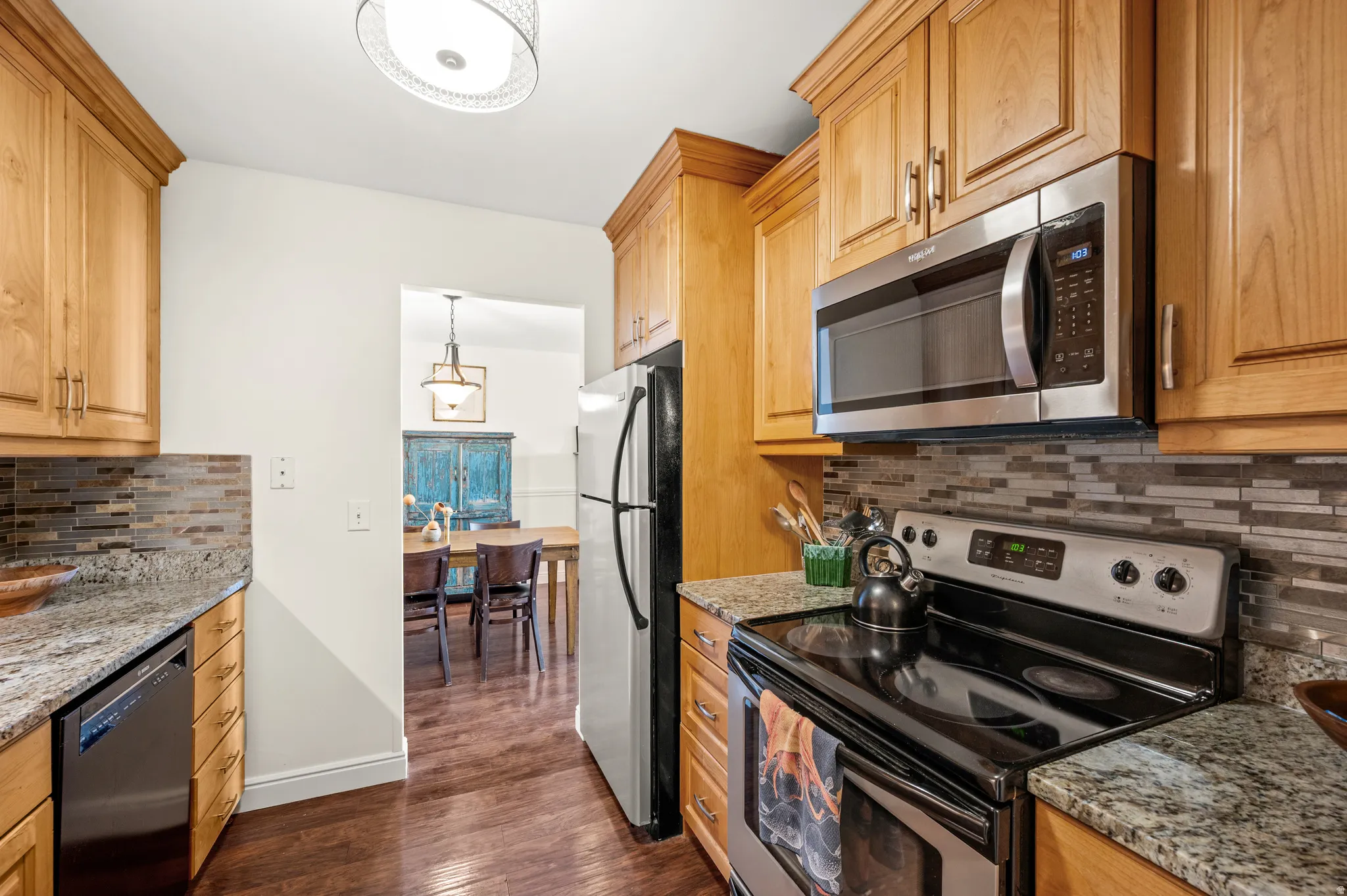 Kitchen with stainless steel appliances, decorative backsplash, light stone countertops, and dark wood finished floors