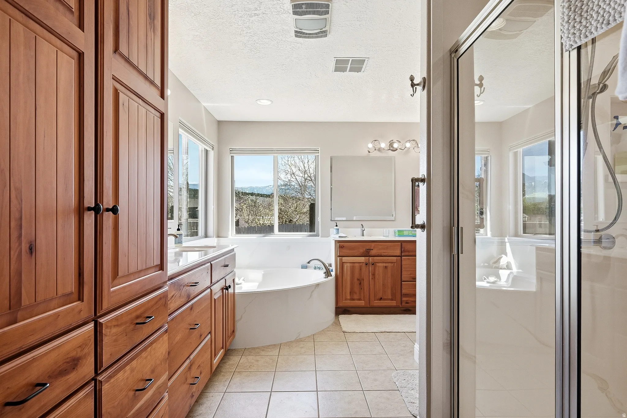Bathroom featuring a shower stall, vanity, light tile patterned floors, a bath, and a textured ceiling