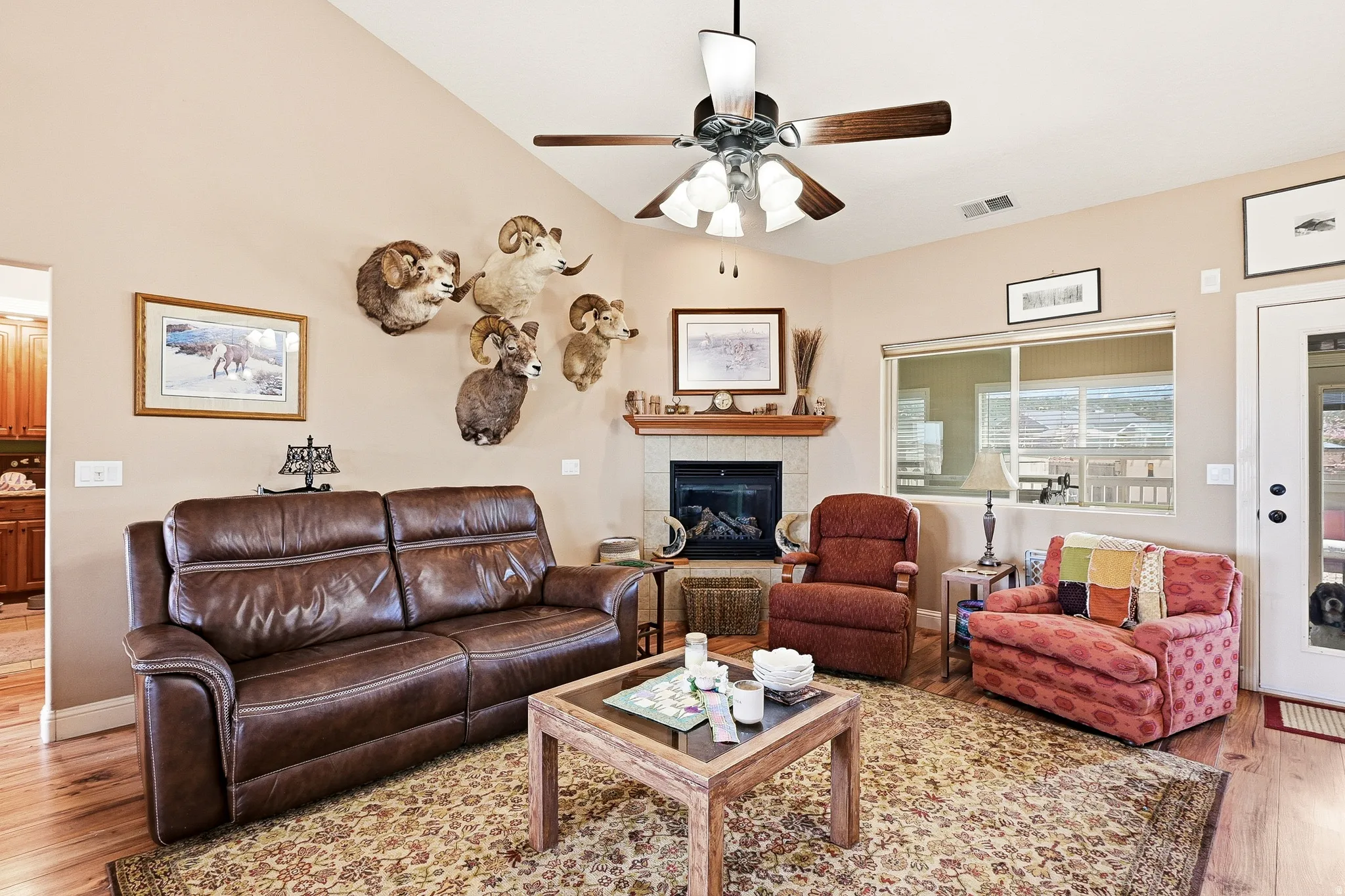 Living room with light wood finished floors, a tiled fireplace, ceiling fan, and vaulted ceiling