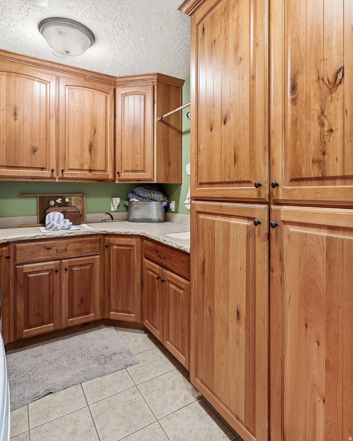 Kitchen featuring a textured ceiling, light tile patterned floors, wood finish cabinetry, and light stone countertops