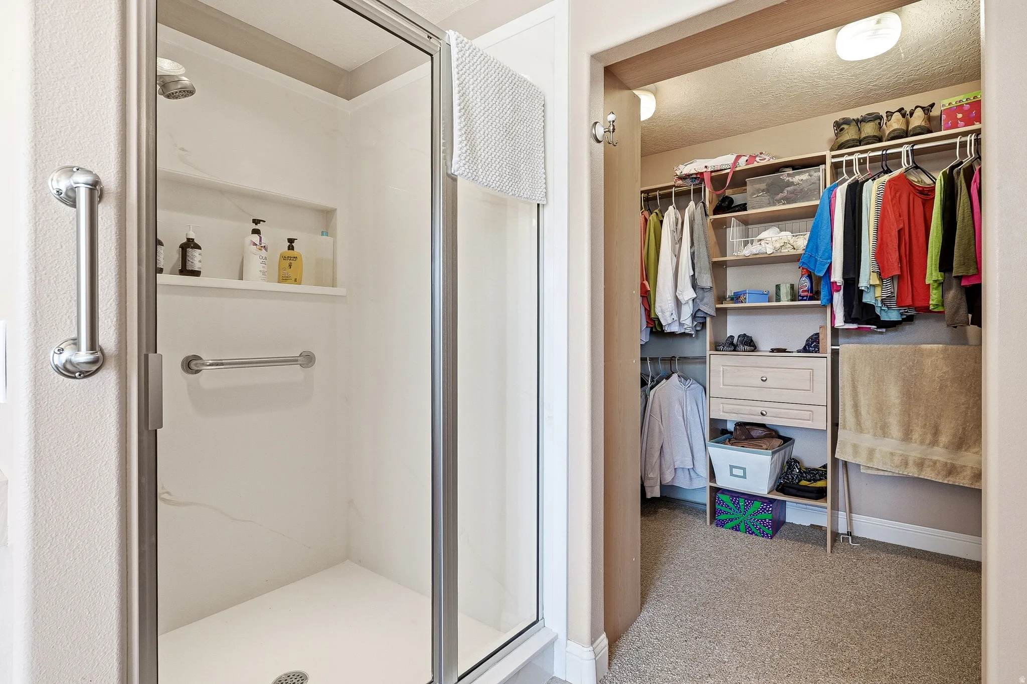 Bathroom featuring a spacious closet, a stall shower, light carpet, and a textured ceiling