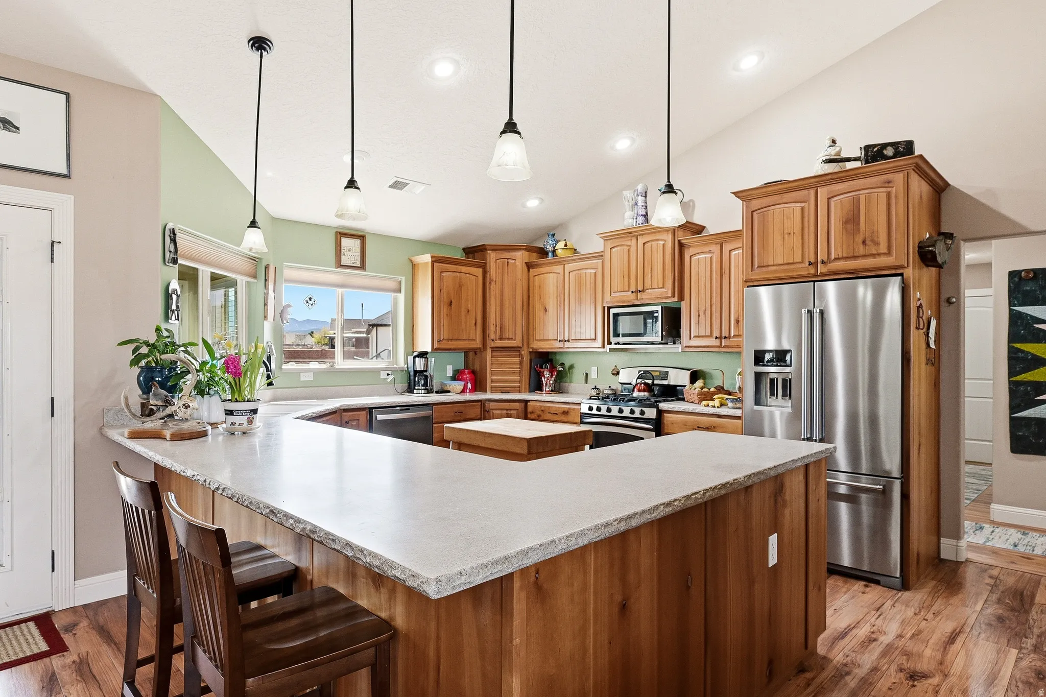 Kitchen with stainless steel appliances, wood finish cabinetry, hanging light fixtures, dark wood finished floors, and lofted ceiling