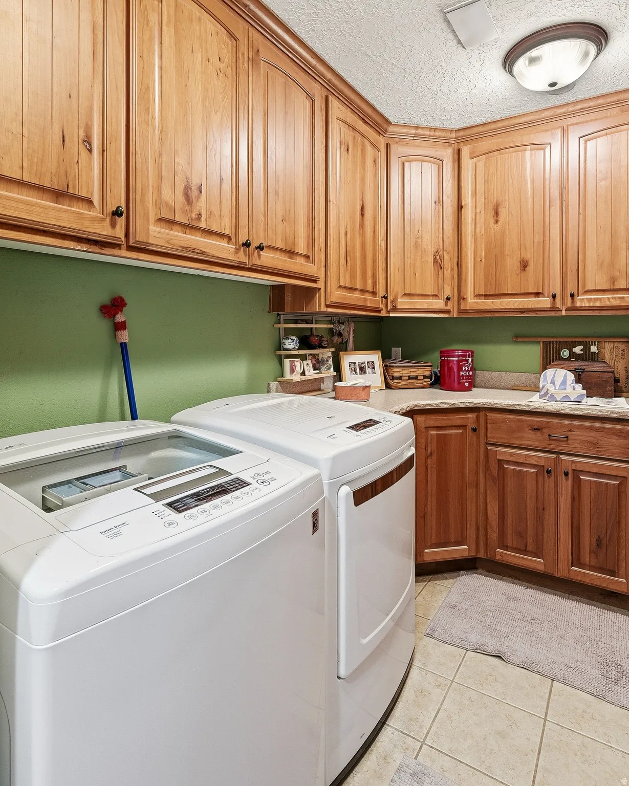 Laundry room featuring a textured ceiling, washing machine and clothes dryer, cabinet space, and light tile patterned floors