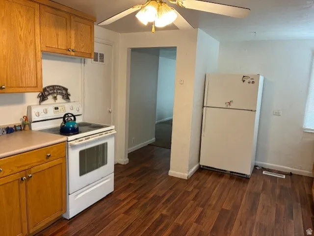 Kitchen with white appliances, light countertops, wood finish cabinetry, ceiling fan, and dark wood finished floors