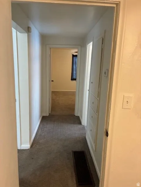 Hall featuring dark colored carpet and baseboards
