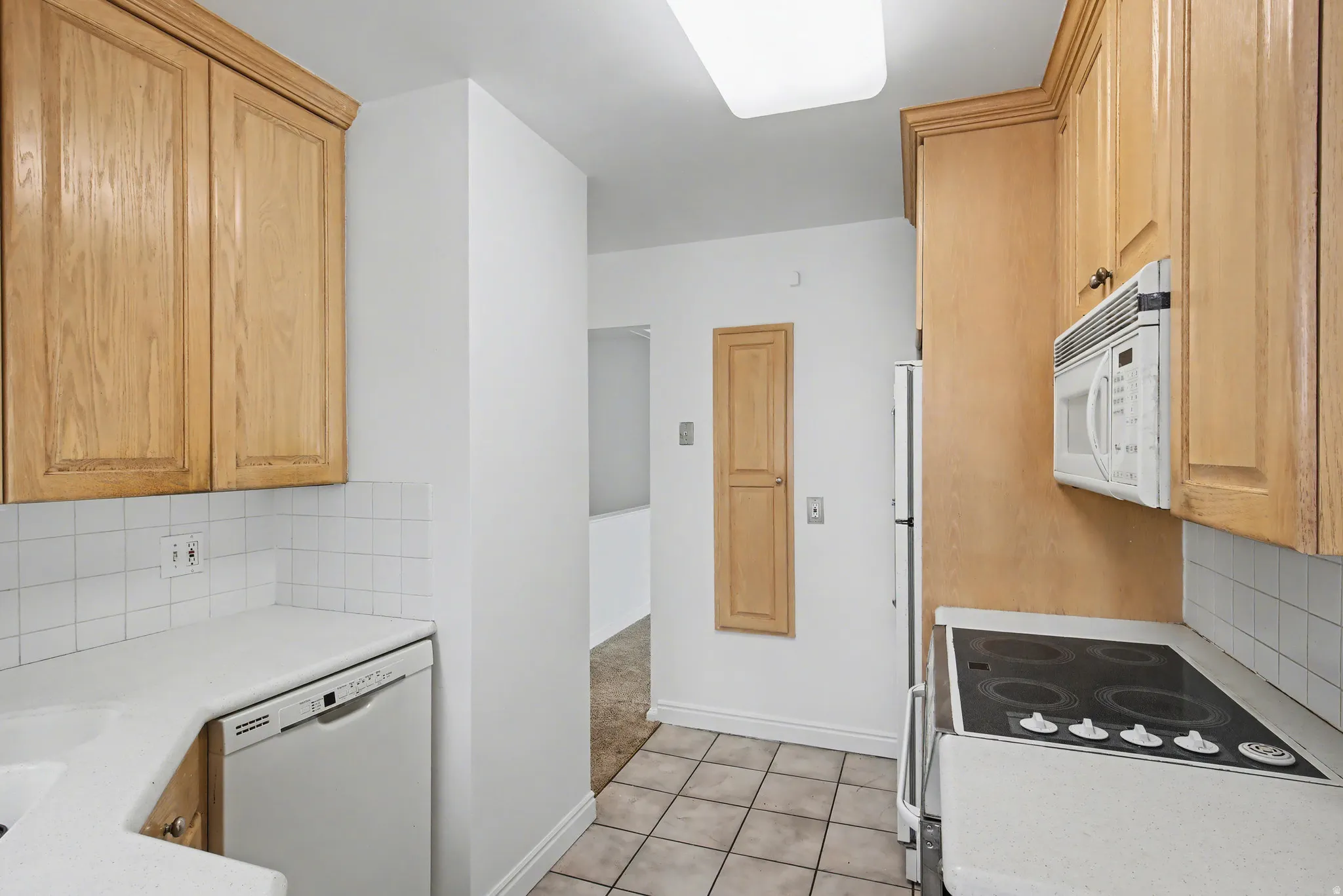 Kitchen with backsplash, light countertops, white appliances, light carpet, and light wood finish cabinetry