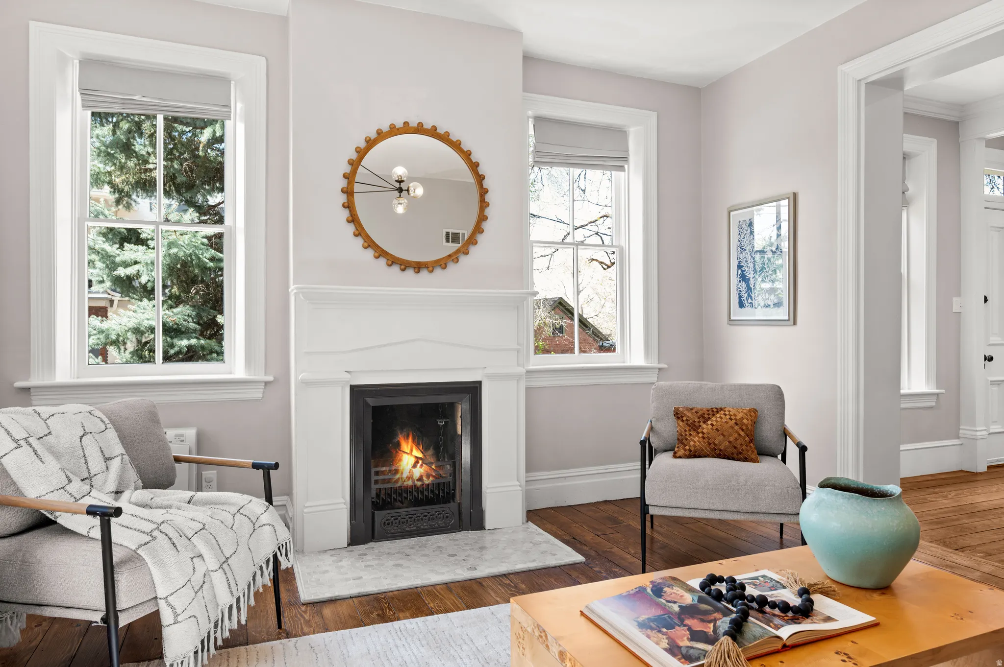 Living area with dark wood-style floors, a warm lit fireplace, and healthy amount of natural light