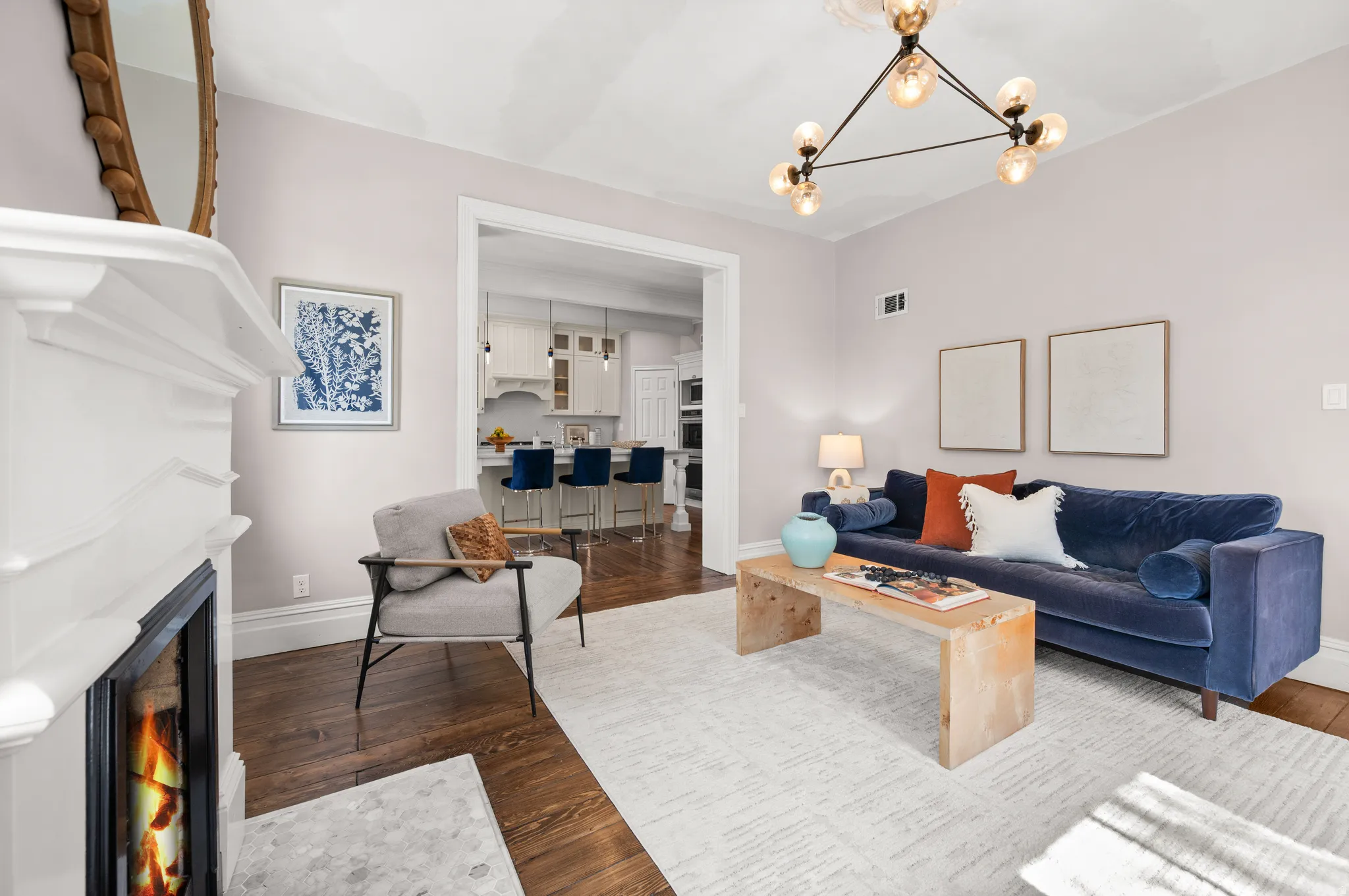 Living room with a lit fireplace, hanging lights, dark wood-style flooring, and wine cooler