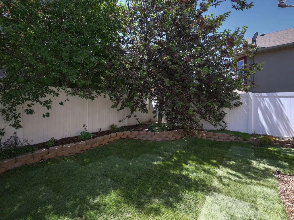 Expansive backyard featuring a manicured lawn, established trees, and a white privacy fence