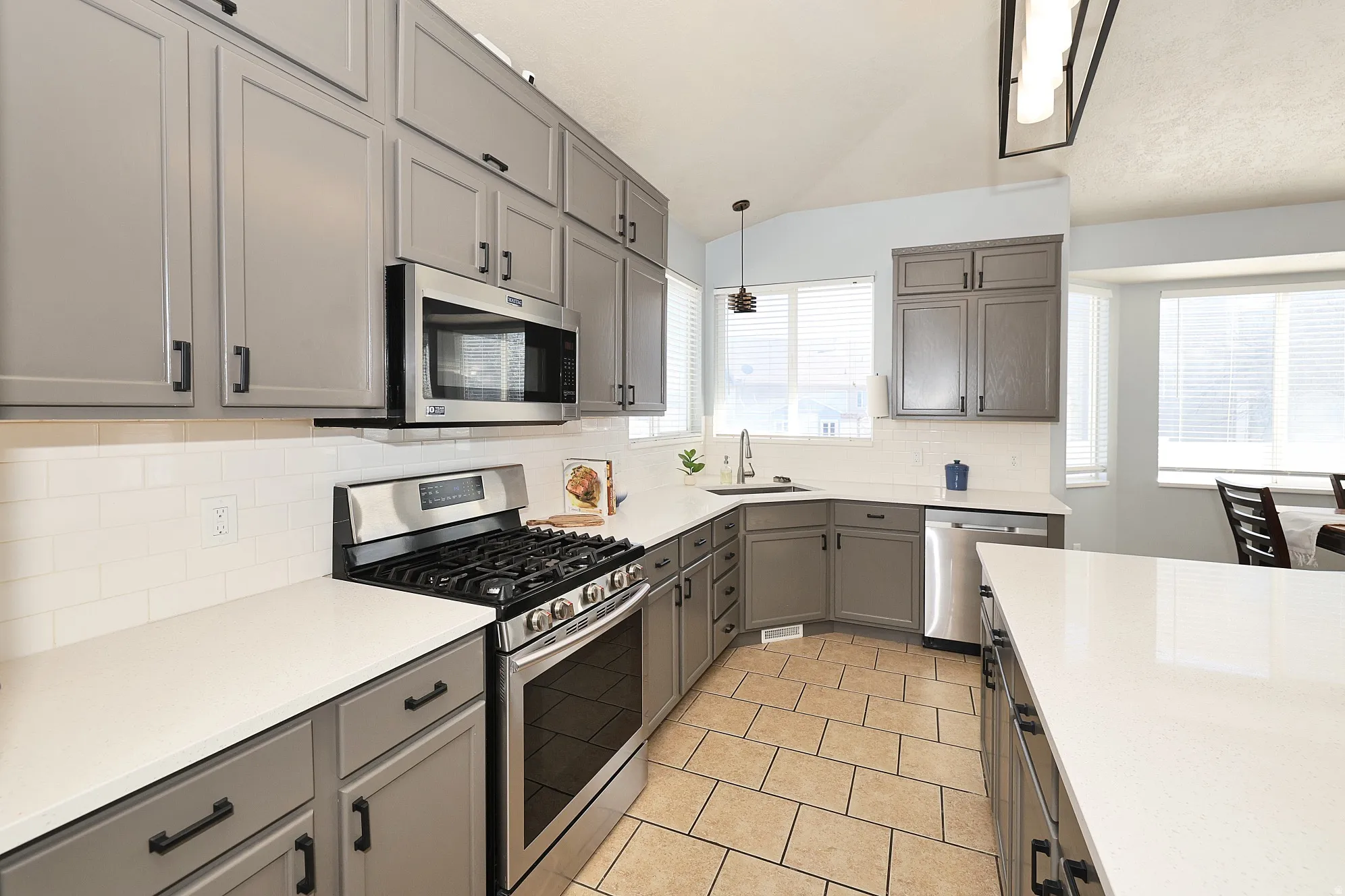 Kitchen with stainless steel appliances, gray cabinetry, decorative backsplash, light tile patterned floors, and hanging light fixtures