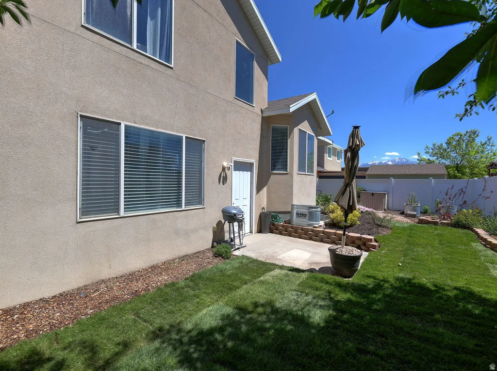 Spacious backyard featuring a manicured lawn, concrete patio, and garden beds with brick retaining walls