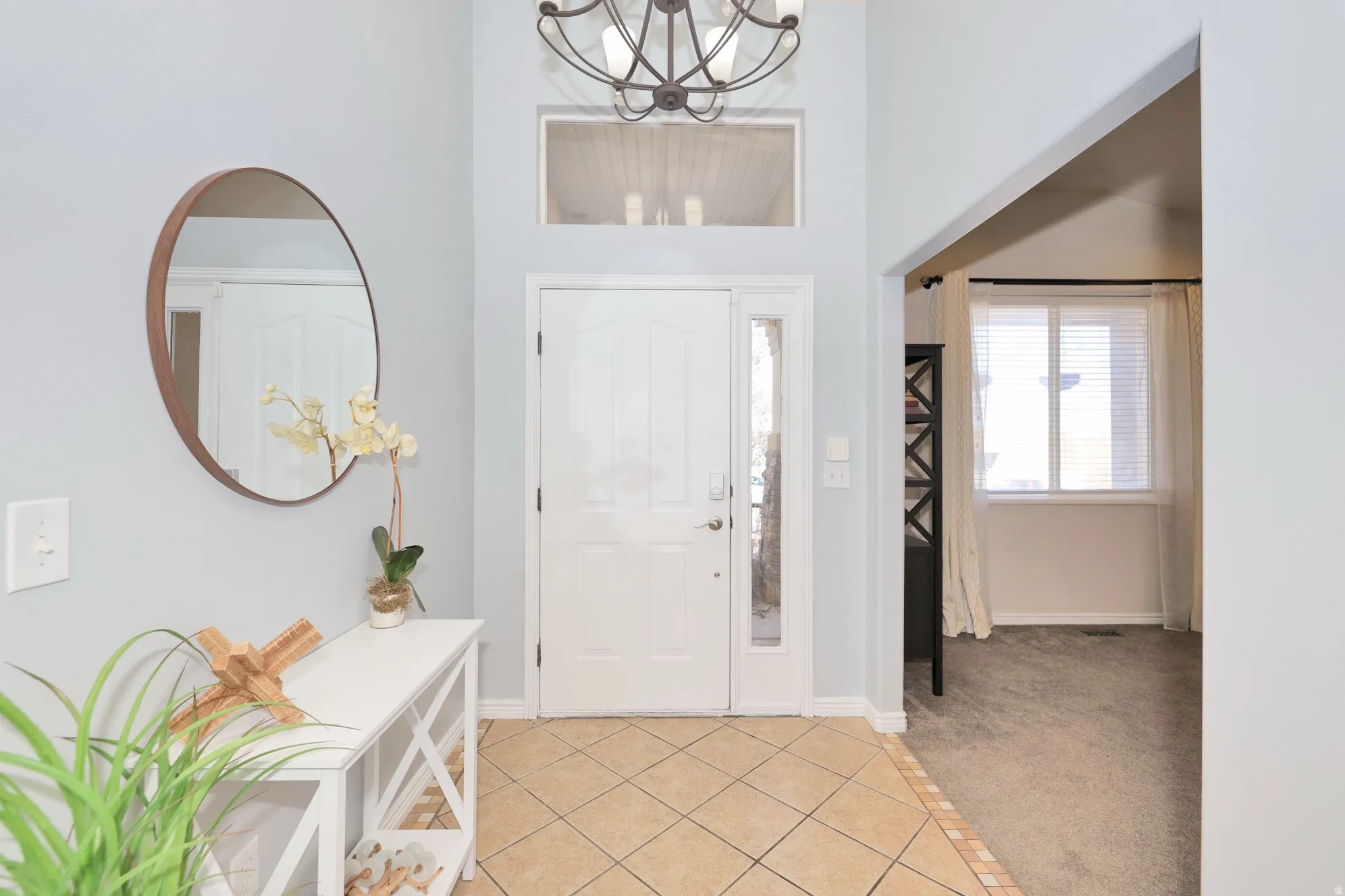 Foyer entrance featuring light tile patterned floors, hanging lights, light carpet, and a high ceiling