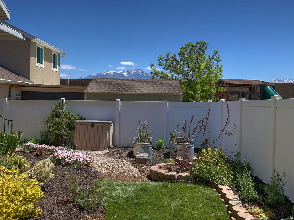 Backyard featuring a privacy fence, landscaped flower beds, a manicured lawn, and a stone-lined planter
