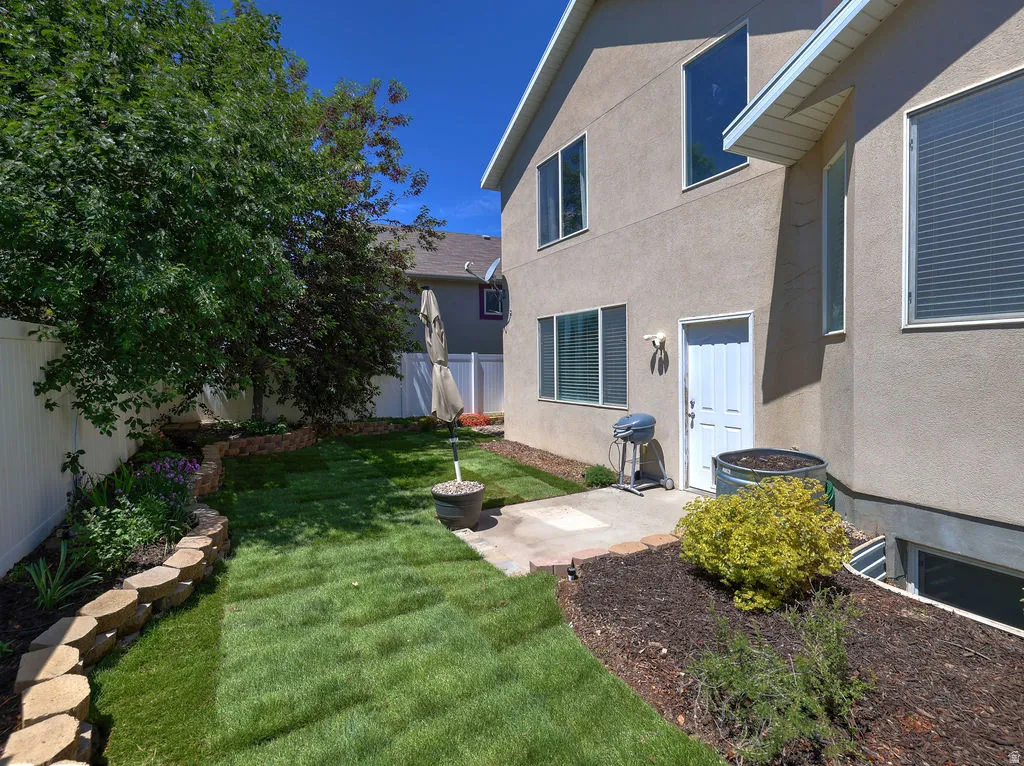 Private backyard featuring manicured lawn, tiered retaining walls, mature trees, and a concrete patio