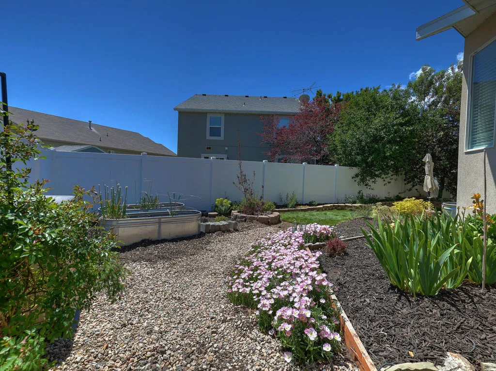 Landscaped backyard featuring a gravel pathway, raised garden beds, and vibrant floral plantings