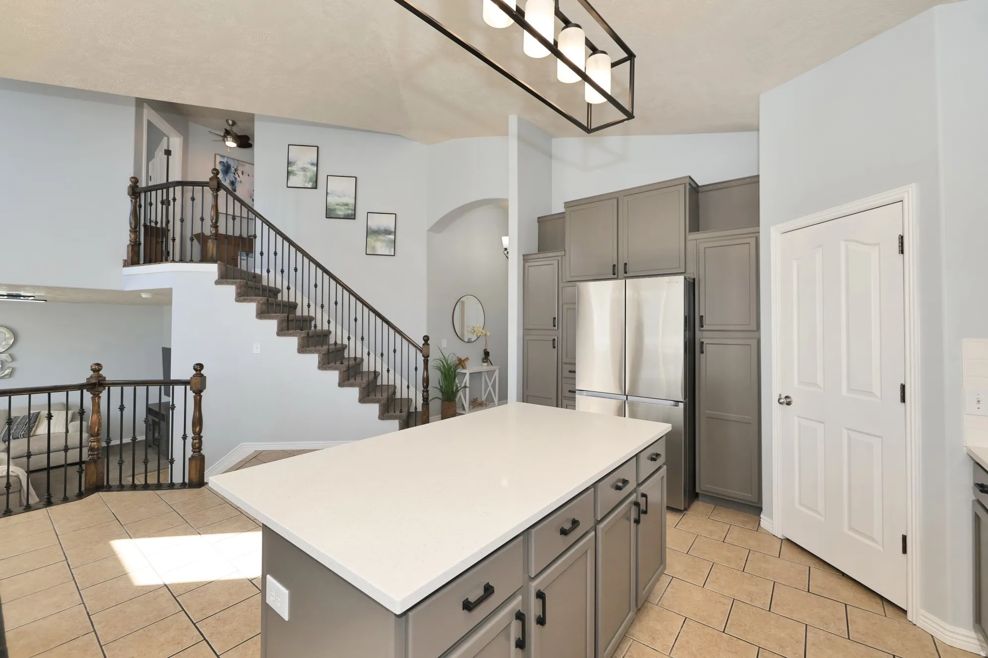 Kitchen featuring freestanding refrigerator, gray cabinetry, light countertops, a center island, and a high ceiling