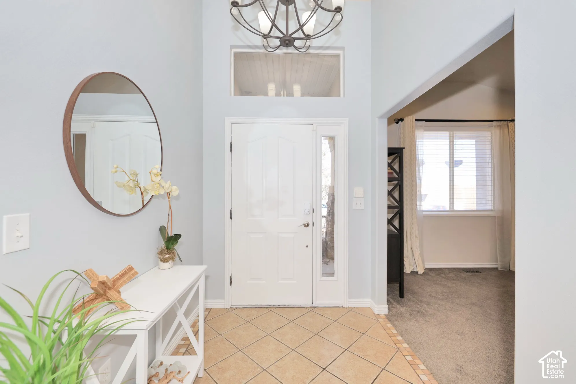 Foyer entrance featuring light tile patterned floors, hanging lights, light carpet, and a high ceiling