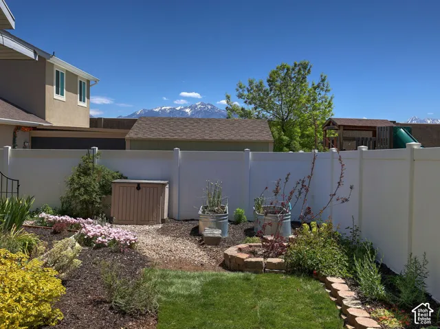 Backyard featuring a privacy fence, landscaped flower beds, a manicured lawn, and a stone-lined planter