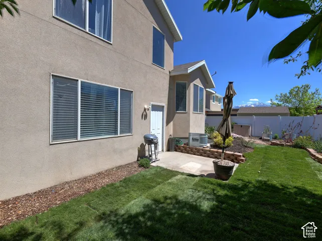 Spacious backyard featuring a manicured lawn, concrete patio, and garden beds with brick retaining walls