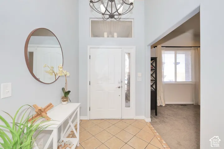 Foyer entrance featuring light tile patterned floors, hanging lights, light carpet, and a high ceiling