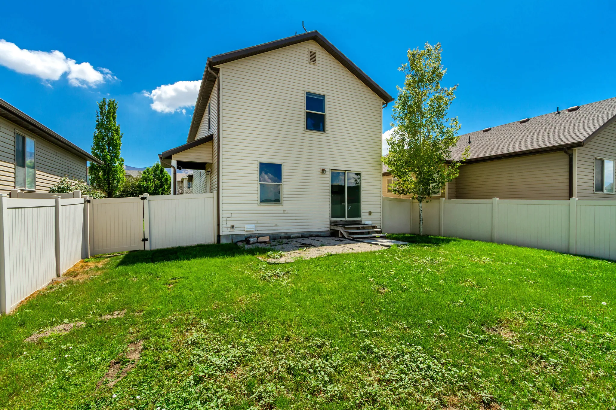 Expansive rear yard featuring green lawn, a privacy fence, and a patio with steps
