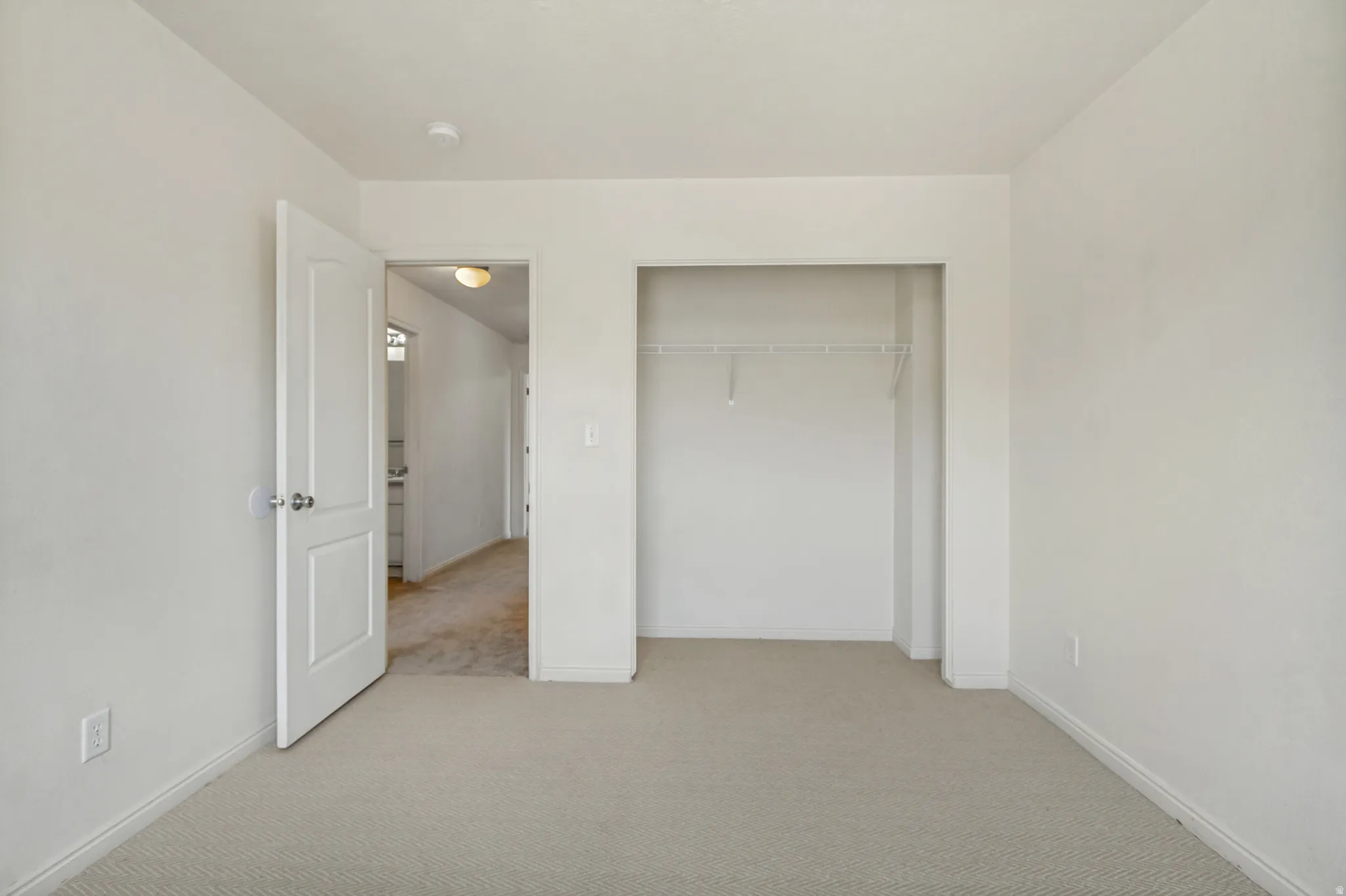 Neutral-toned carpeting paired with white walls, a white interior door, and a built-in closet featuring wire shelving