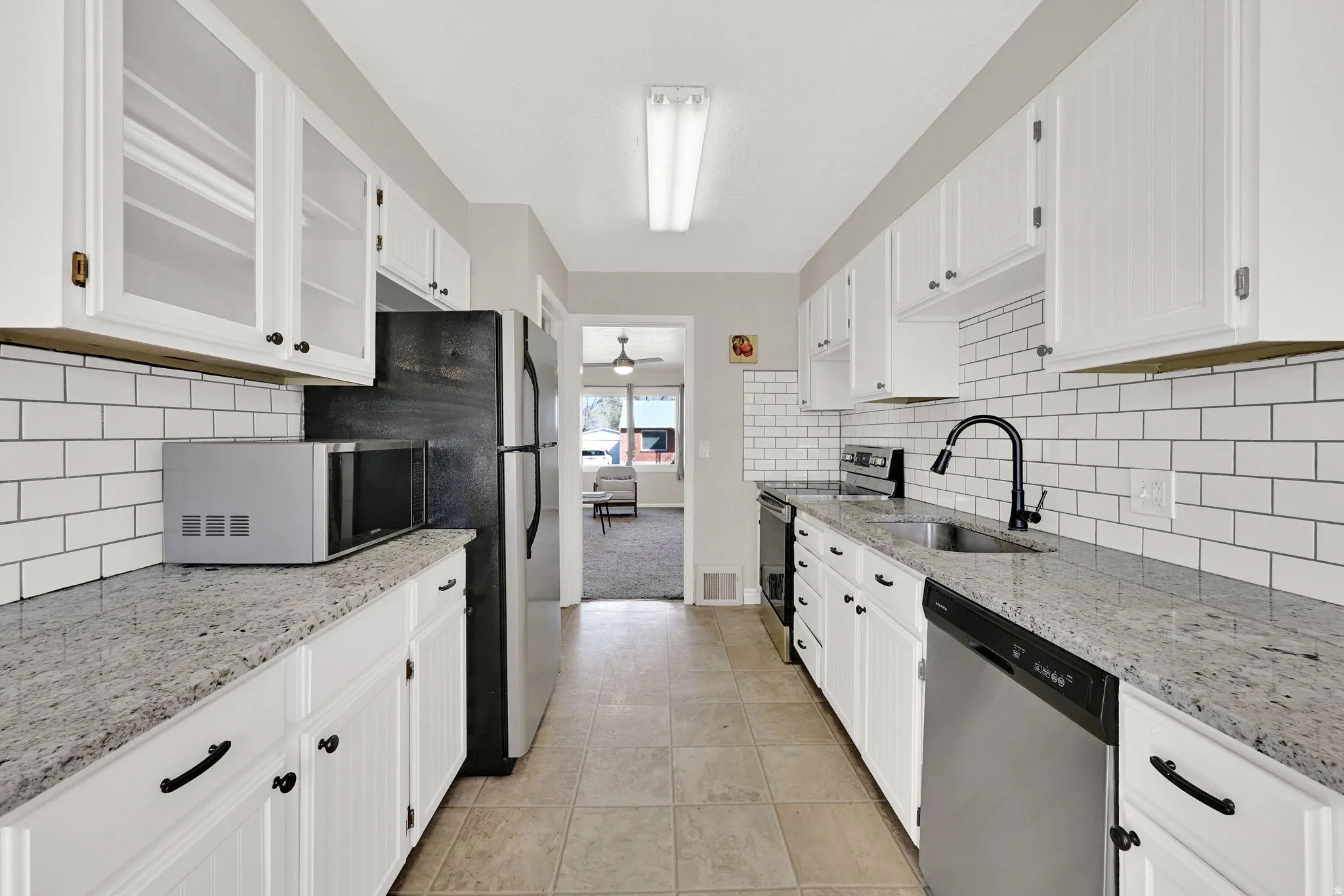 Kitchen with light stone counters, stainless steel appliances, white cabinetry, glass insert cabinets, and light tile patterned floors