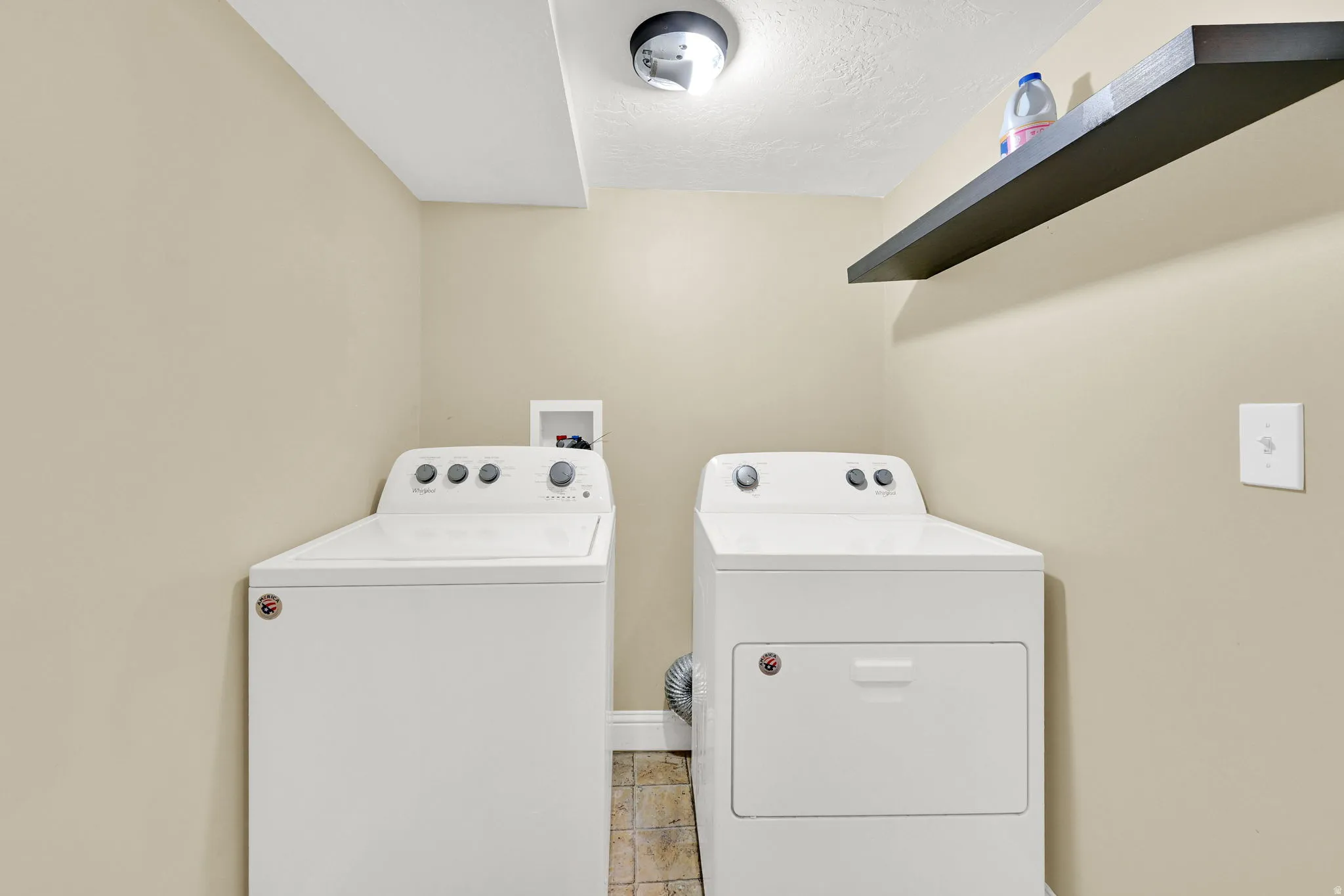 Laundry room featuring independent washer and dryer, light tile patterned floors, and a textured ceiling
