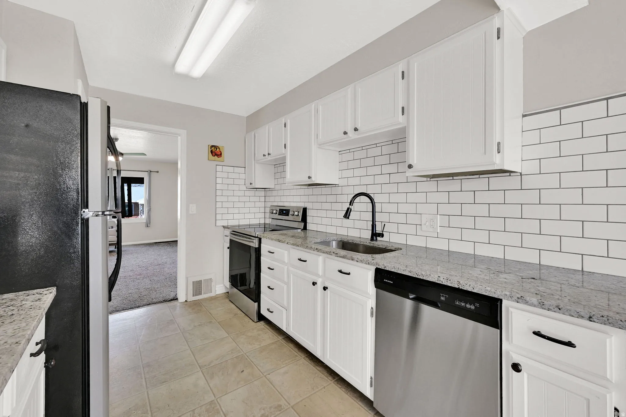 Kitchen featuring stainless steel appliances, light stone countertops, white cabinets, light tile patterned flooring, and tasteful backsplash