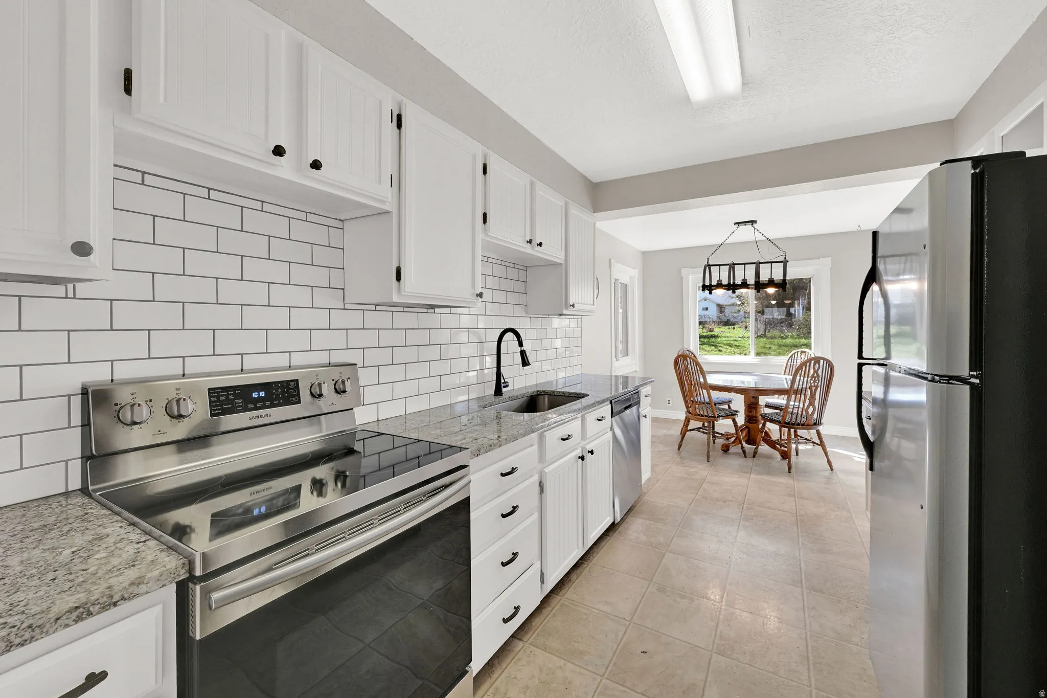 Kitchen with stainless steel appliances, white cabinets, light stone counters, light tile patterned floors, and tasteful backsplash