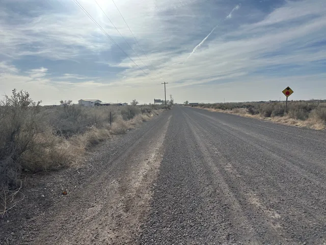 View of dirt / gravel road with a view of rural / pastoral area and traffic signs