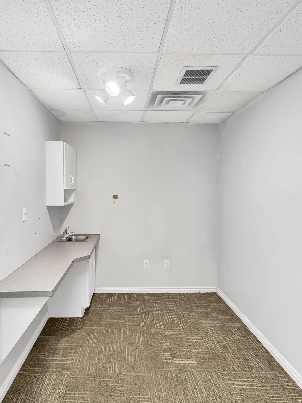 Unfurnished office with a drop ceiling and dark colored carpet