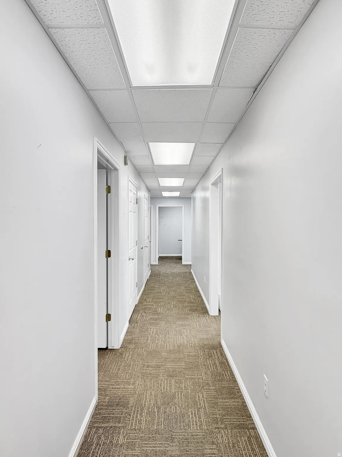 Hallway featuring a paneled ceiling and dark colored carpet