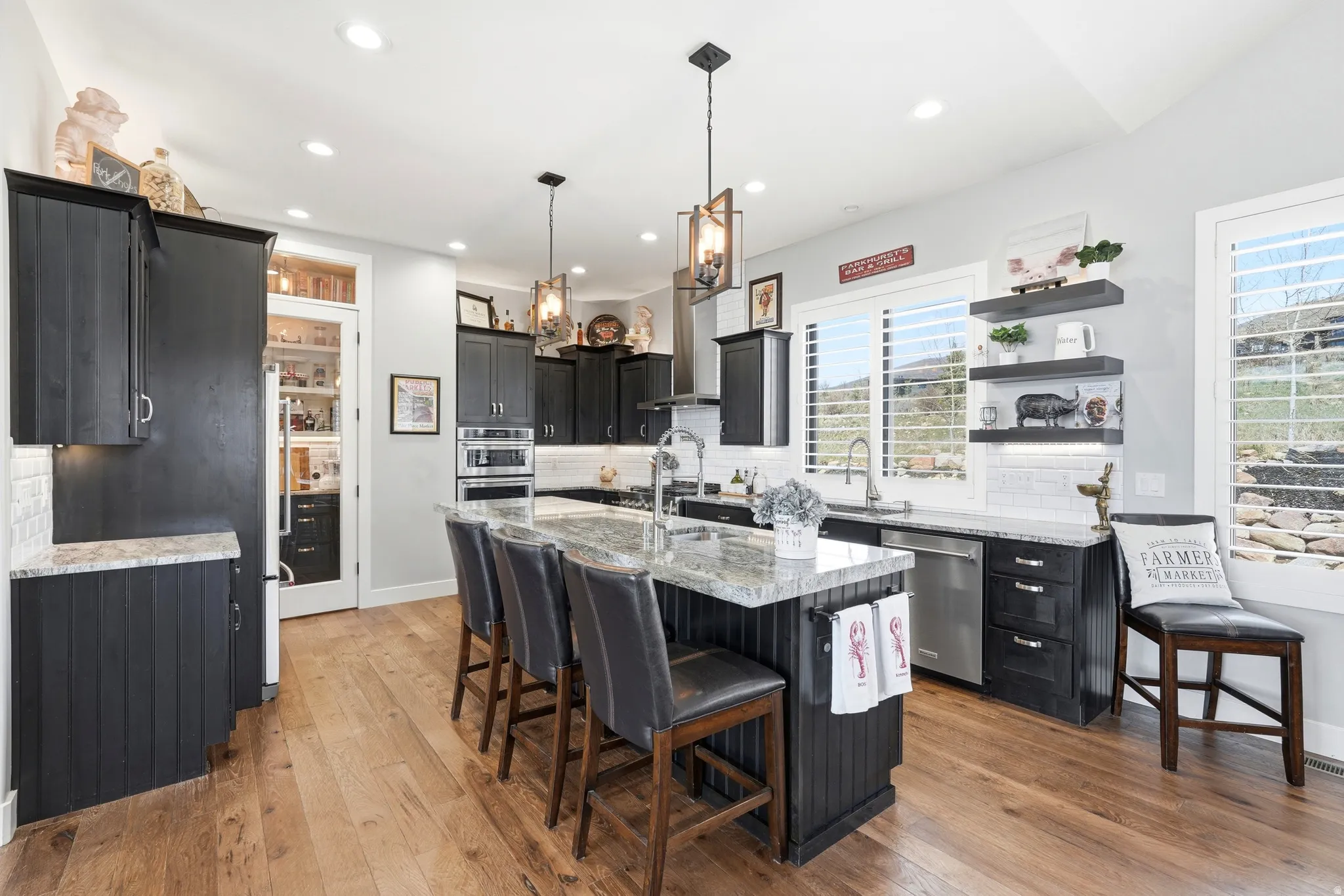 Kitchen with dark cabinetry, a kitchen breakfast bar, light stone counters, decorative backsplash, and an island with sink