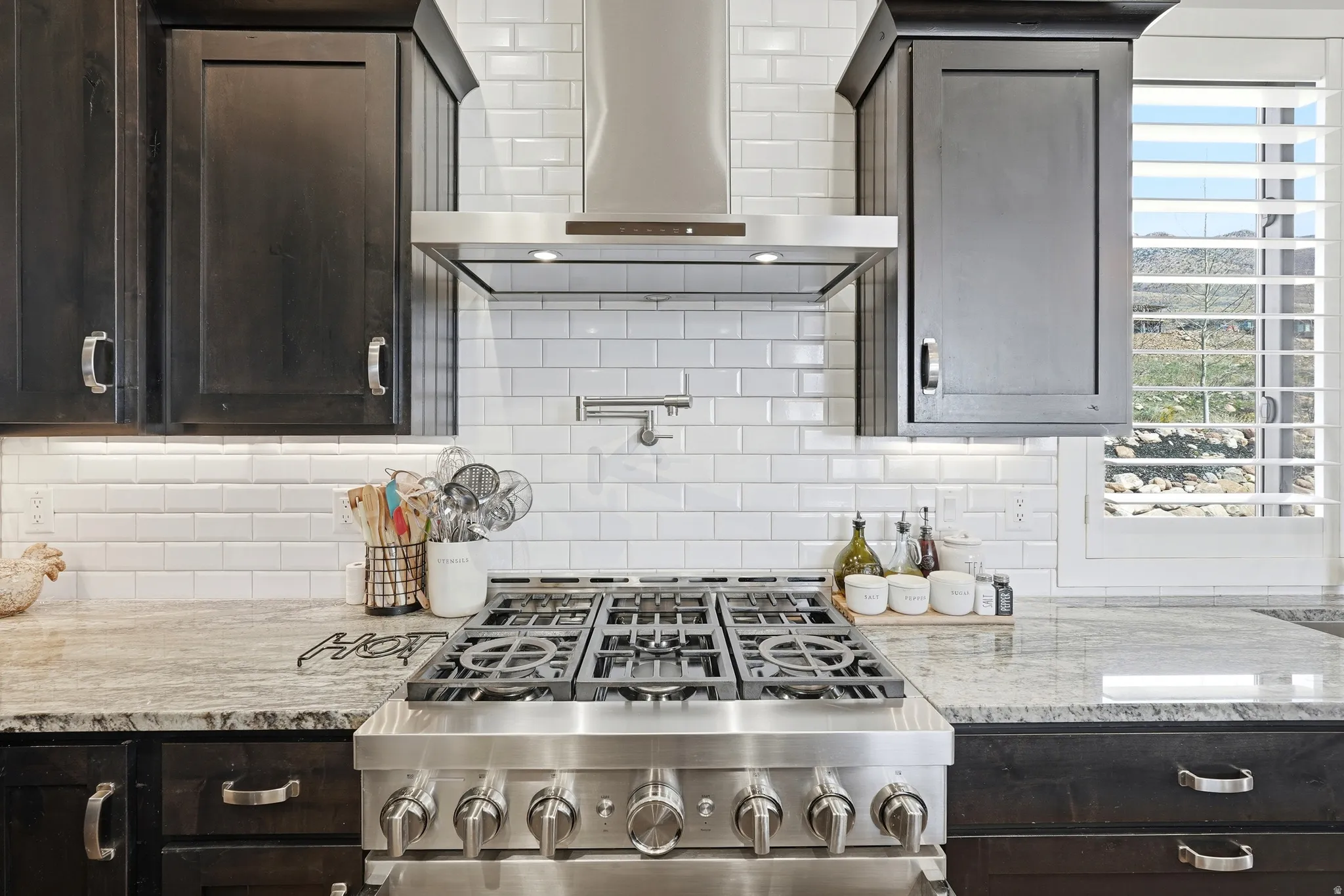 Kitchen with dark wood finish cabinets, light stone counters, gas stove, and backsplash