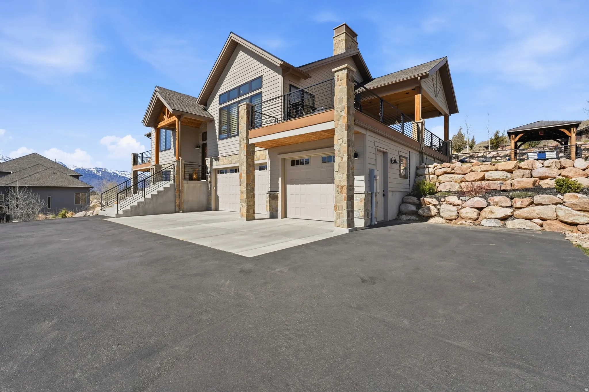 View of side of home with asphalt driveway, an attached garage, stone siding, a mountain view, and a chimney