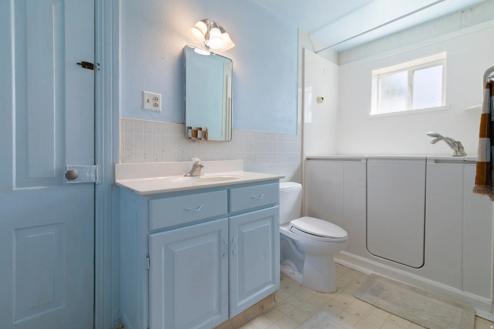 Bathroom with vanity, tile walls, a wainscoted wall, and light floors