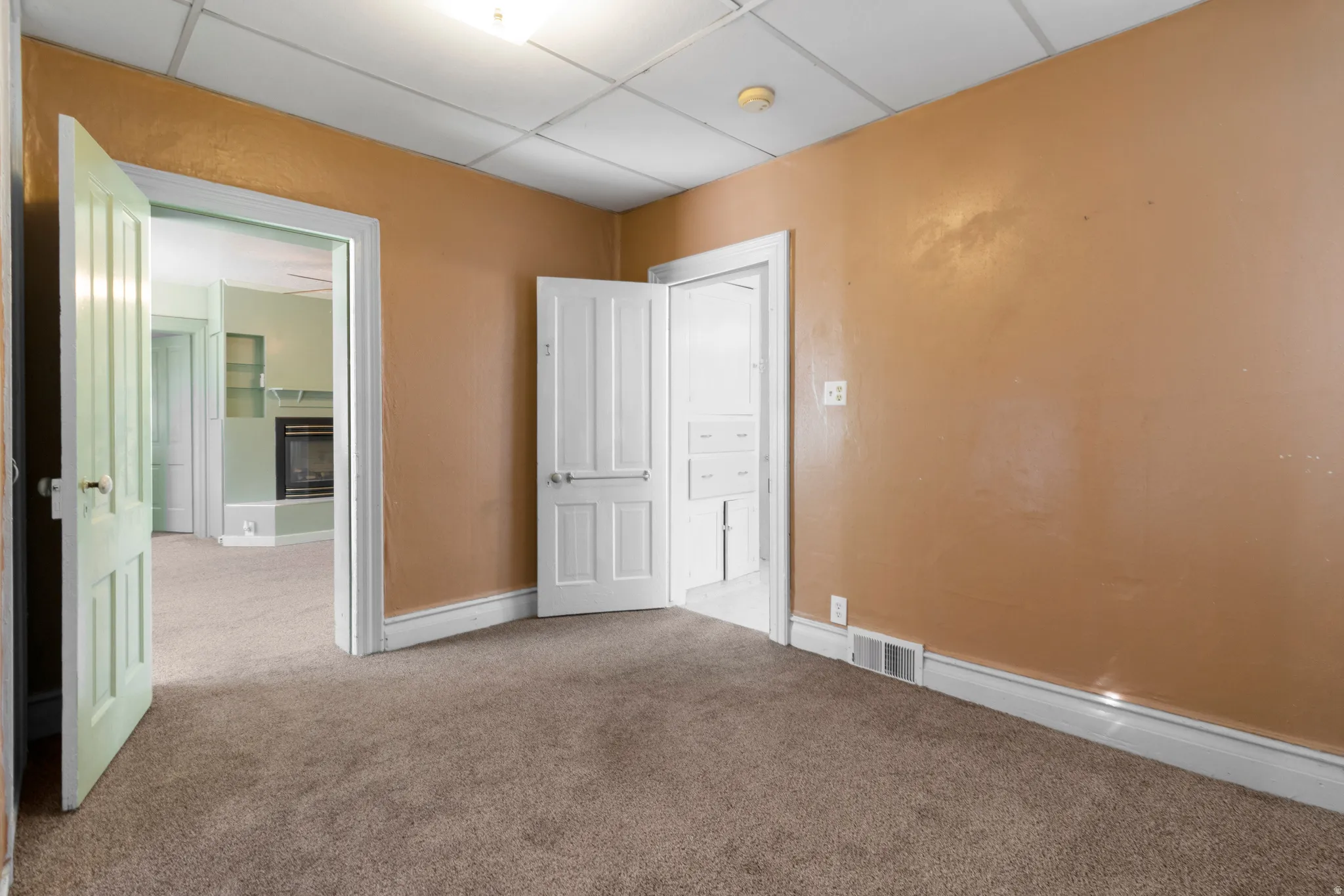 Unfurnished bedroom featuring carpet, a glass covered fireplace, and a paneled ceiling