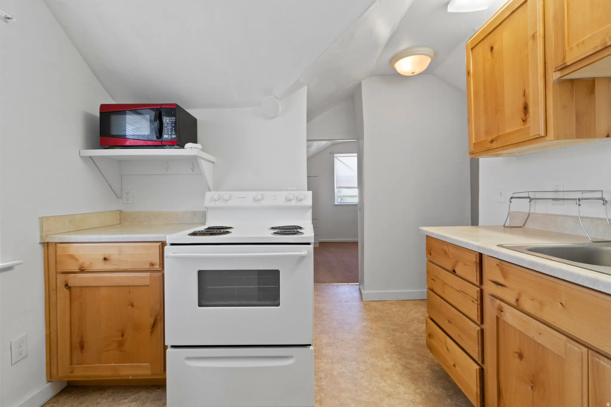 Kitchen featuring white range with electric stovetop, light countertops, lofted ceiling, and light wood finish cabinets